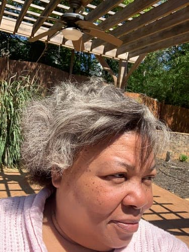 Customer photographed outdoors in a garden, with short grey curly hair